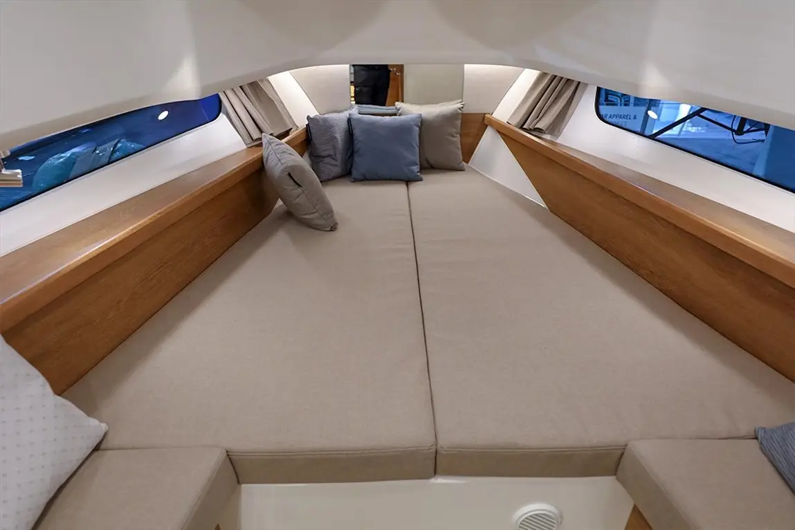 Modern boat interior with beige cushions, wooden trim, and several blue pillows, showcasing a cozy sleeping area.